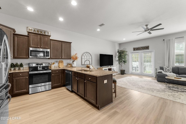 kitchen with light wood-type flooring, appliances with stainless steel finishes, sink, a breakfast bar, and kitchen peninsula