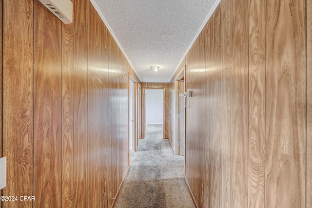 corridor with wooden walls, a textured ceiling, and carpet floors