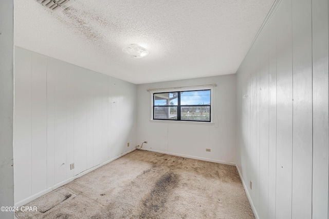 empty room featuring wood walls, light colored carpet, and a textured ceiling