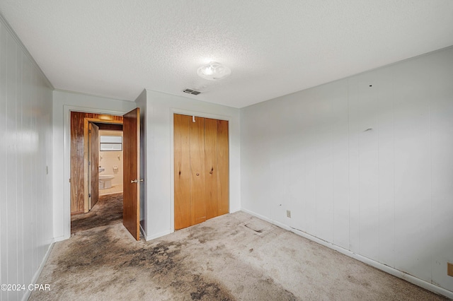 unfurnished bedroom with carpet flooring, wooden walls, a textured ceiling, and a closet