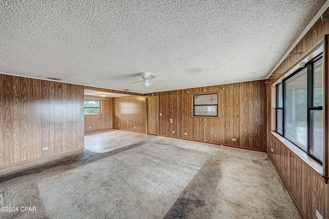 empty room featuring a textured ceiling, light carpet, ceiling fan, and wooden walls