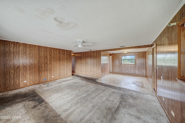 carpeted empty room featuring wooden walls, a textured ceiling, and ceiling fan