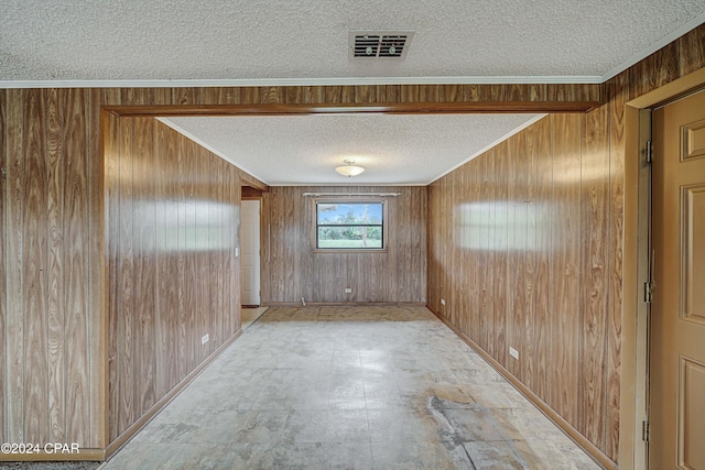 empty room with wood walls, a textured ceiling, and crown molding