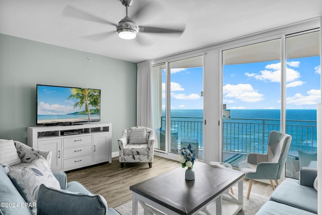 living room with expansive windows, ceiling fan, a water view, and light wood-style floors