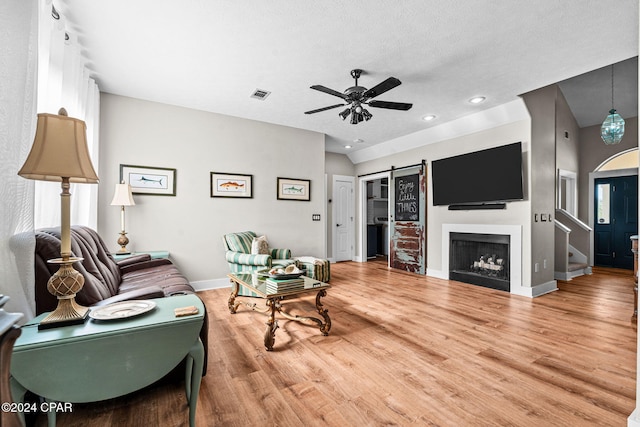 living room with a textured ceiling, wood-type flooring, a barn door, and ceiling fan