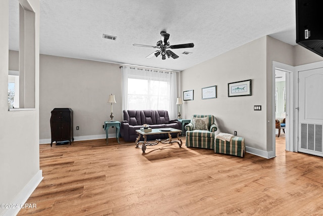 living room featuring light wood-type flooring, a textured ceiling, and ceiling fan