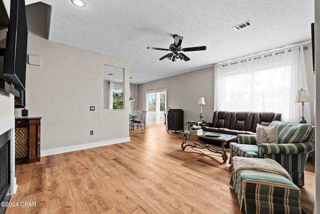 living room with light wood-type flooring, a textured ceiling, and ceiling fan