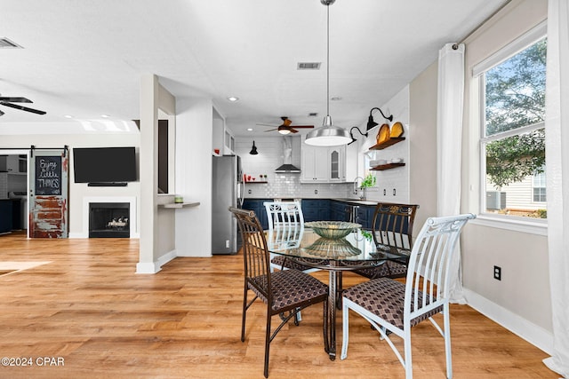 dining area featuring light hardwood / wood-style floors, a barn door, sink, and ceiling fan