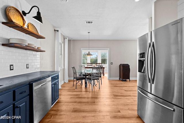 kitchen with decorative backsplash, a textured ceiling, blue cabinetry, light wood-type flooring, and appliances with stainless steel finishes