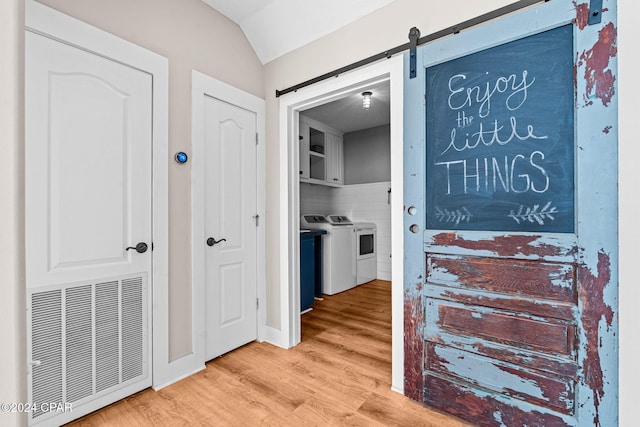 hall with tile walls, separate washer and dryer, light hardwood / wood-style floors, and a barn door