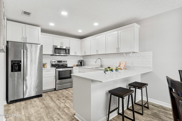 kitchen with white cabinetry, sink, stainless steel appliances, a breakfast bar area, and light wood-type flooring