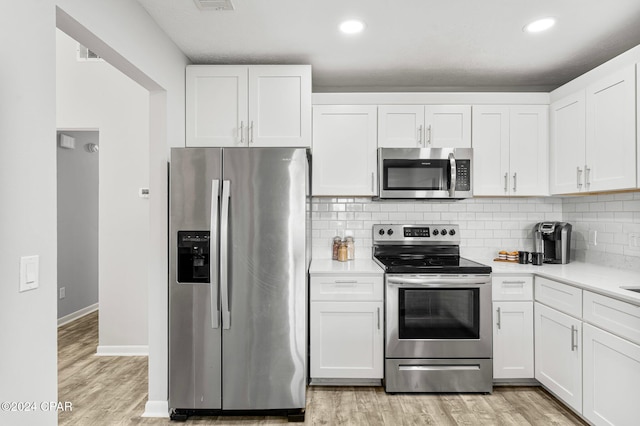 kitchen with white cabinets, backsplash, light hardwood / wood-style floors, and stainless steel appliances