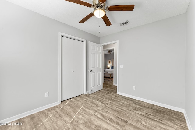 unfurnished bedroom with ceiling fan, a closet, light hardwood / wood-style floors, and a textured ceiling