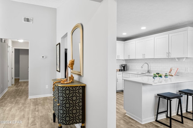 kitchen with sink, light hardwood / wood-style floors, a textured ceiling, a breakfast bar, and white cabinets