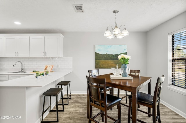 dining room featuring sink, wood-type flooring, a textured ceiling, and an inviting chandelier