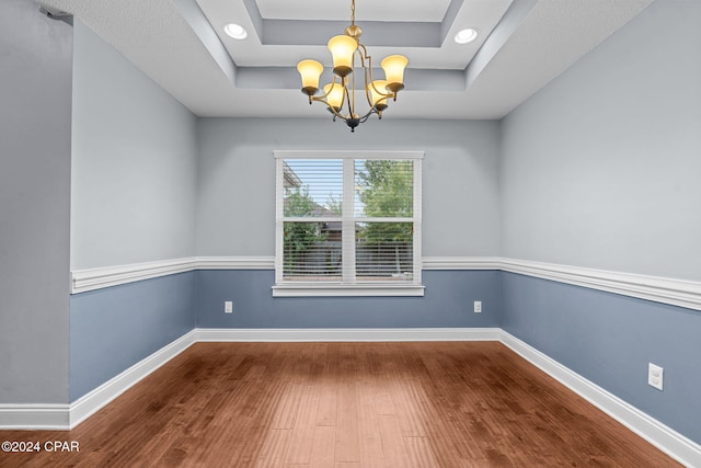 spare room featuring hardwood / wood-style floors, a chandelier, and a tray ceiling