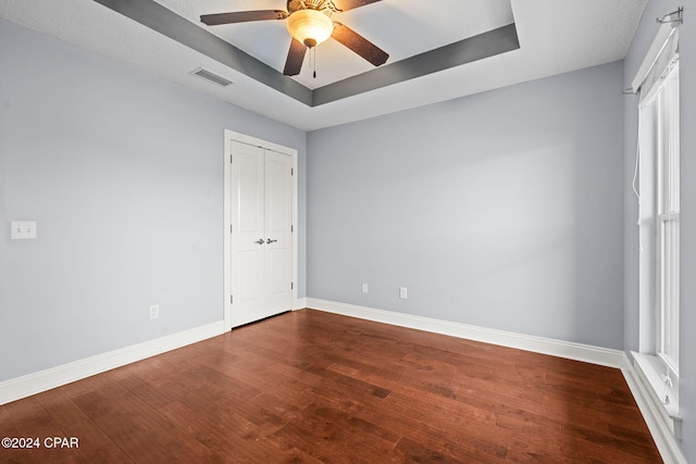 unfurnished bedroom with a tray ceiling, a closet, ceiling fan, and hardwood / wood-style floors