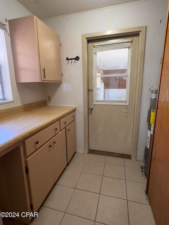 kitchen with electric water heater, light tile patterned flooring, a textured ceiling, and cream cabinetry