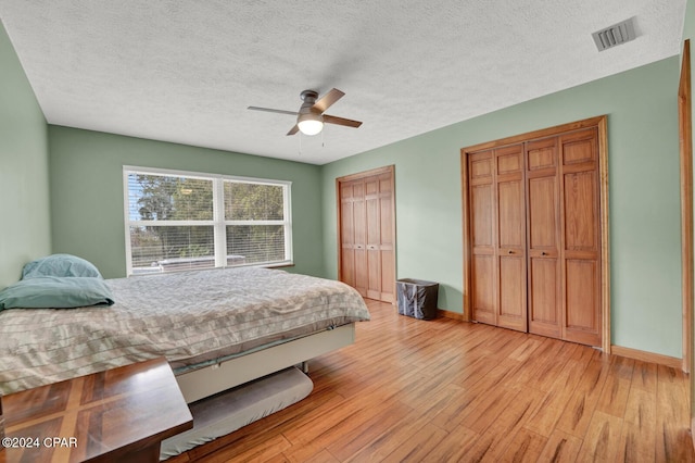 bedroom featuring light wood-type flooring, two closets, a textured ceiling, and ceiling fan