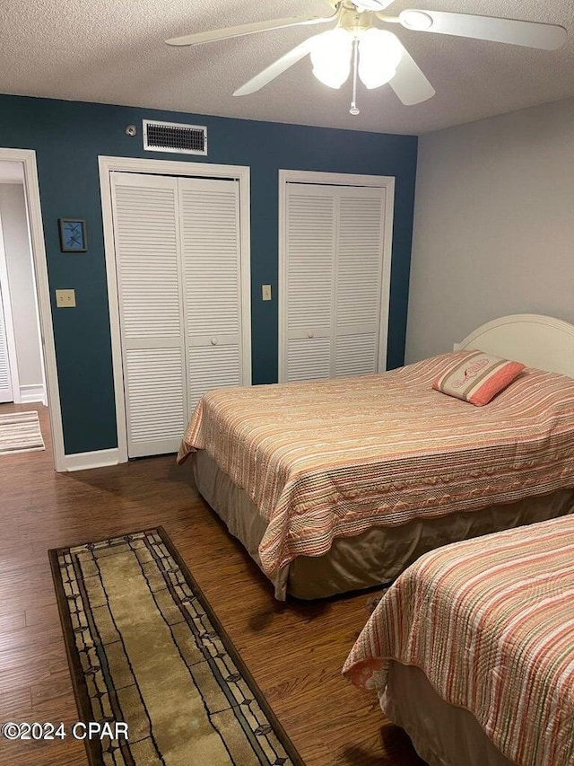 bedroom featuring two closets, ceiling fan, wood-type flooring, and a textured ceiling