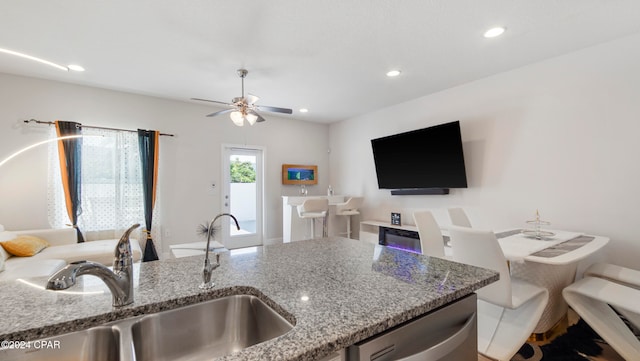 kitchen featuring dishwasher, sink, ceiling fan, and stone counters