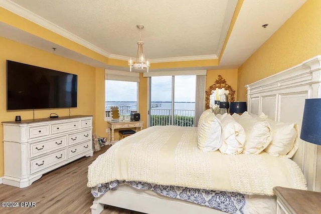 bedroom with hardwood / wood-style flooring, a tray ceiling, a chandelier, and crown molding