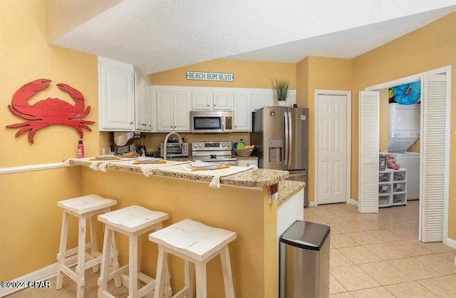 kitchen with a kitchen bar, kitchen peninsula, stainless steel appliances, light stone countertops, and white cabinets