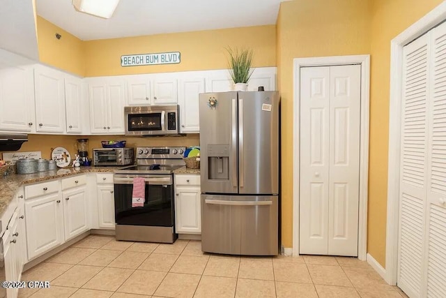 kitchen featuring stainless steel appliances, stone countertops, light tile patterned floors, and white cabinets