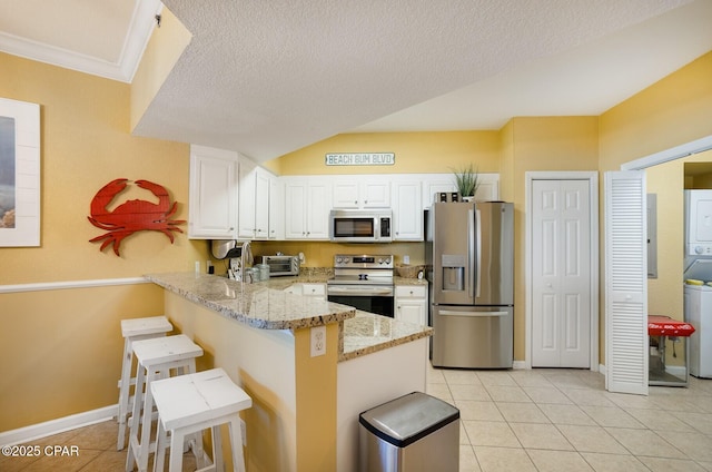 kitchen featuring white cabinets, a kitchen bar, stacked washer / drying machine, kitchen peninsula, and stainless steel appliances