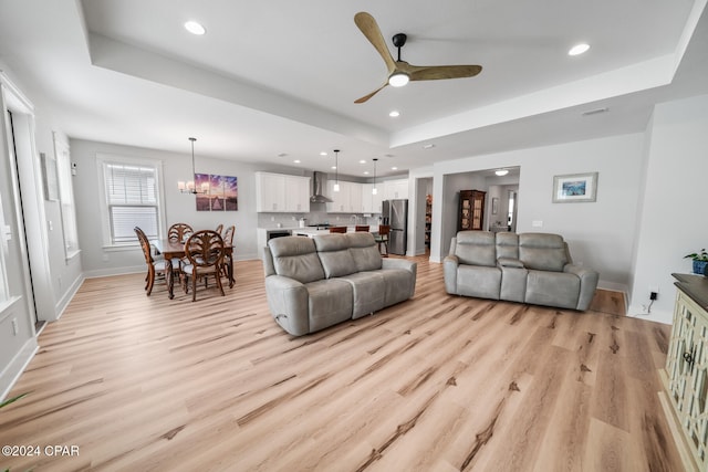 living room with ceiling fan with notable chandelier, light hardwood / wood-style flooring, and a tray ceiling