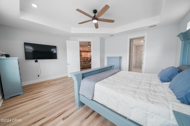 bedroom with ensuite bathroom, a tray ceiling, ceiling fan, and light hardwood / wood-style flooring