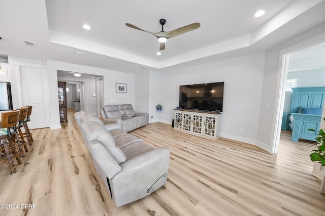 living room featuring ceiling fan, a tray ceiling, and light hardwood / wood-style floors