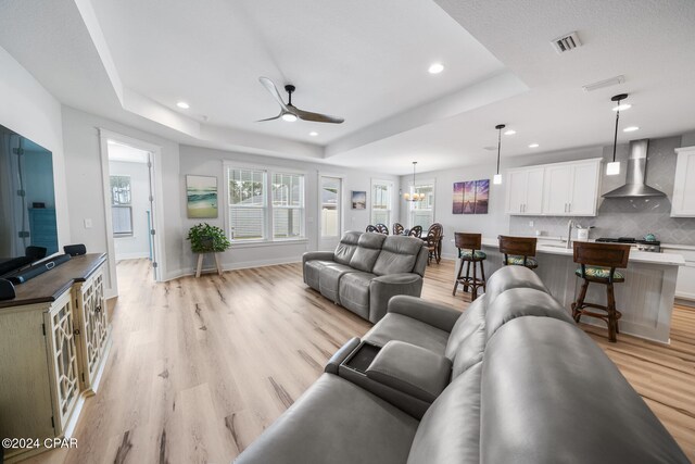 living room featuring ceiling fan with notable chandelier, a raised ceiling, and light hardwood / wood-style flooring