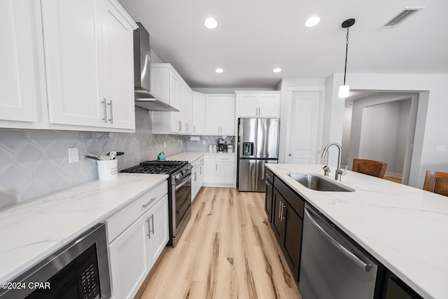kitchen with stainless steel appliances, light hardwood / wood-style floors, sink, wall chimney range hood, and pendant lighting