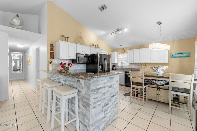 kitchen featuring a kitchen breakfast bar, backsplash, black appliances, dark stone countertops, and white cabinets