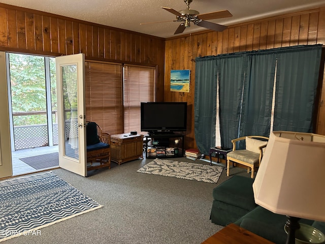 carpeted living room featuring wooden walls, french doors, ceiling fan, and a textured ceiling