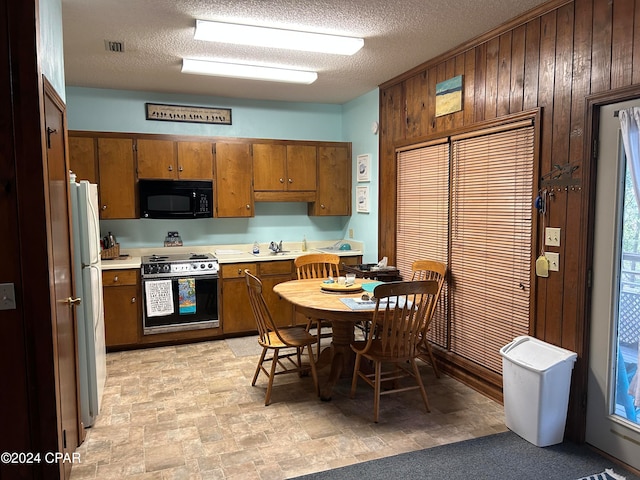 kitchen with stove, a textured ceiling, wooden walls, sink, and white refrigerator