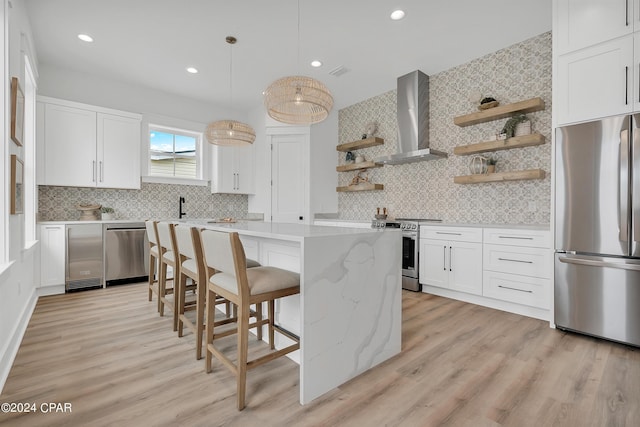 kitchen featuring a breakfast bar, appliances with stainless steel finishes, white cabinets, wall chimney range hood, and backsplash