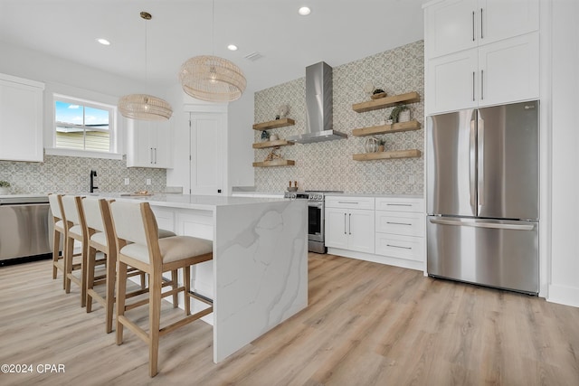 kitchen featuring wall chimney range hood, stainless steel appliances, white cabinets, and a kitchen island