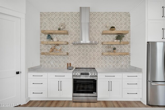 kitchen featuring wall chimney range hood, light hardwood / wood-style flooring, white cabinets, and appliances with stainless steel finishes