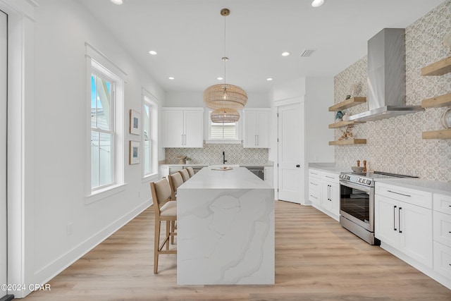 kitchen with appliances with stainless steel finishes, decorative light fixtures, white cabinets, a center island, and wall chimney range hood