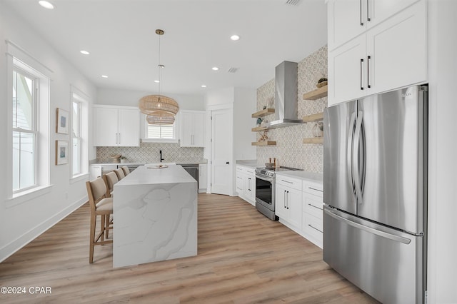 kitchen with a kitchen island, white cabinetry, appliances with stainless steel finishes, and wall chimney range hood