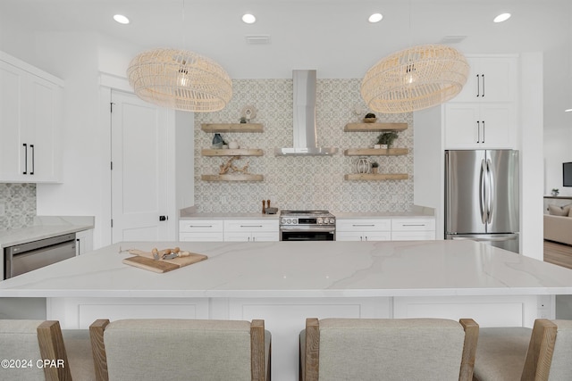 kitchen with stainless steel appliances, decorative light fixtures, a center island, and wall chimney range hood