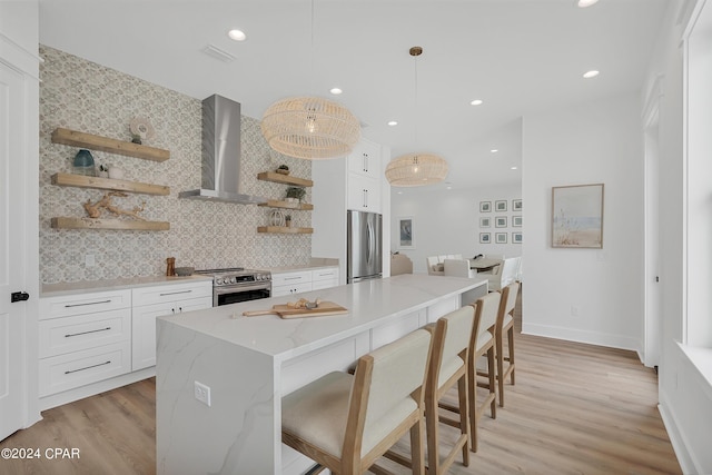 kitchen featuring decorative light fixtures, stainless steel appliances, wall chimney exhaust hood, and white cabinets