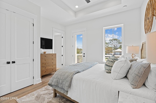 bedroom featuring a raised ceiling, a closet, access to outside, and light hardwood / wood-style flooring