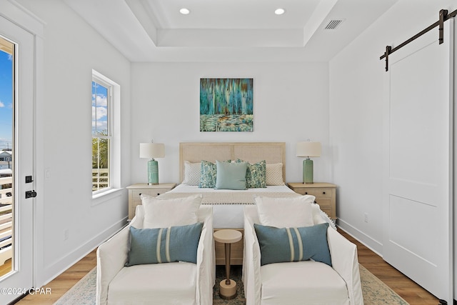 bedroom featuring a barn door, a raised ceiling, and light wood-type flooring