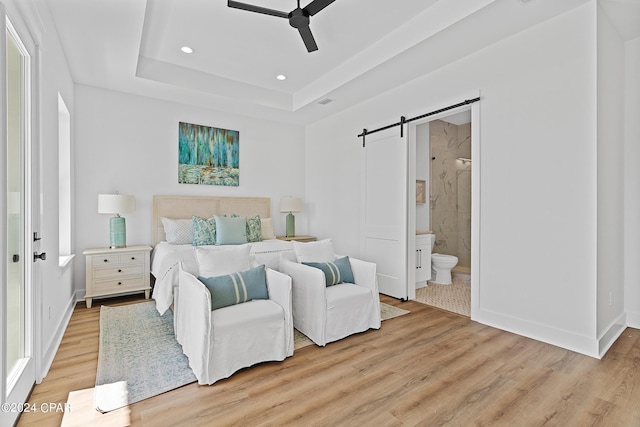 bedroom featuring ensuite bath, a barn door, ceiling fan, and light wood-type flooring