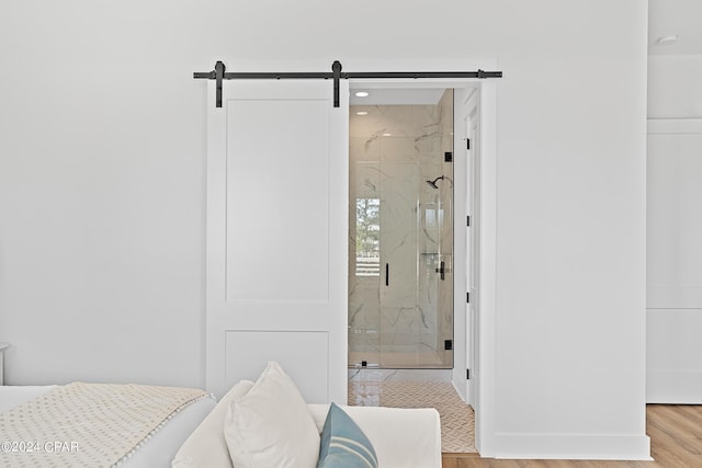 bedroom featuring ensuite bathroom, a barn door, and light hardwood / wood-style flooring