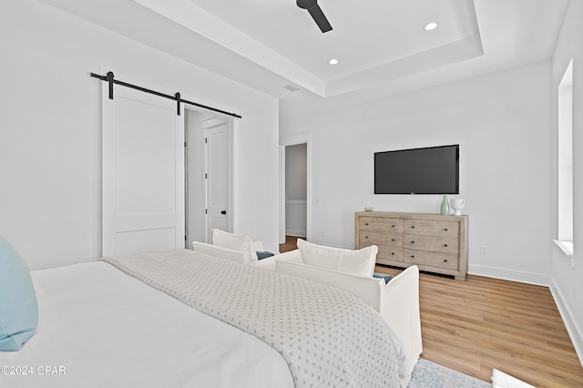 bedroom featuring hardwood / wood-style flooring, a raised ceiling, a barn door, and ceiling fan