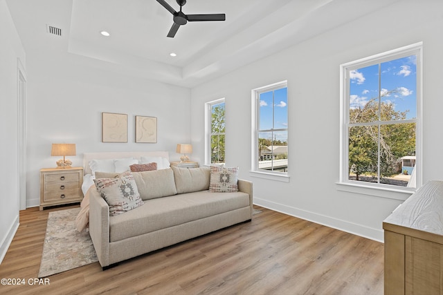 bedroom with light hardwood / wood-style flooring, ceiling fan, and a tray ceiling